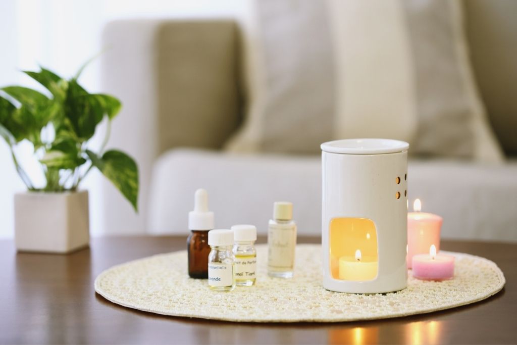 bottles of fragrance oils and a diffuser with lit candle placed on a mat on top of a brown table.